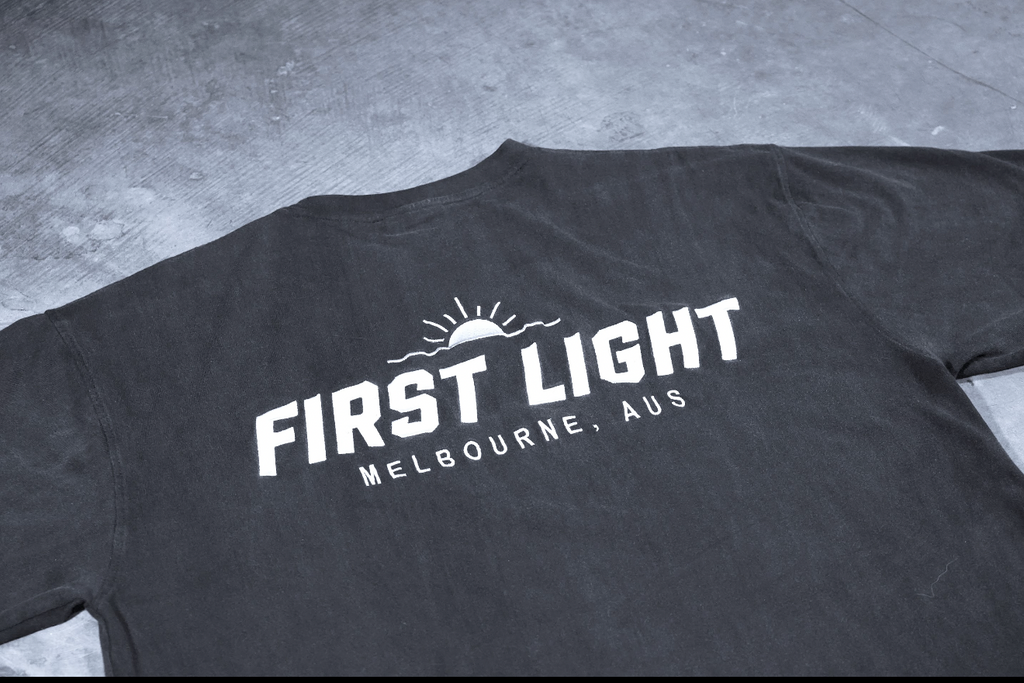 Close-up of the embroidered FIRST LIGHT Melbourne back graphic on the Dawn heavyweight tee