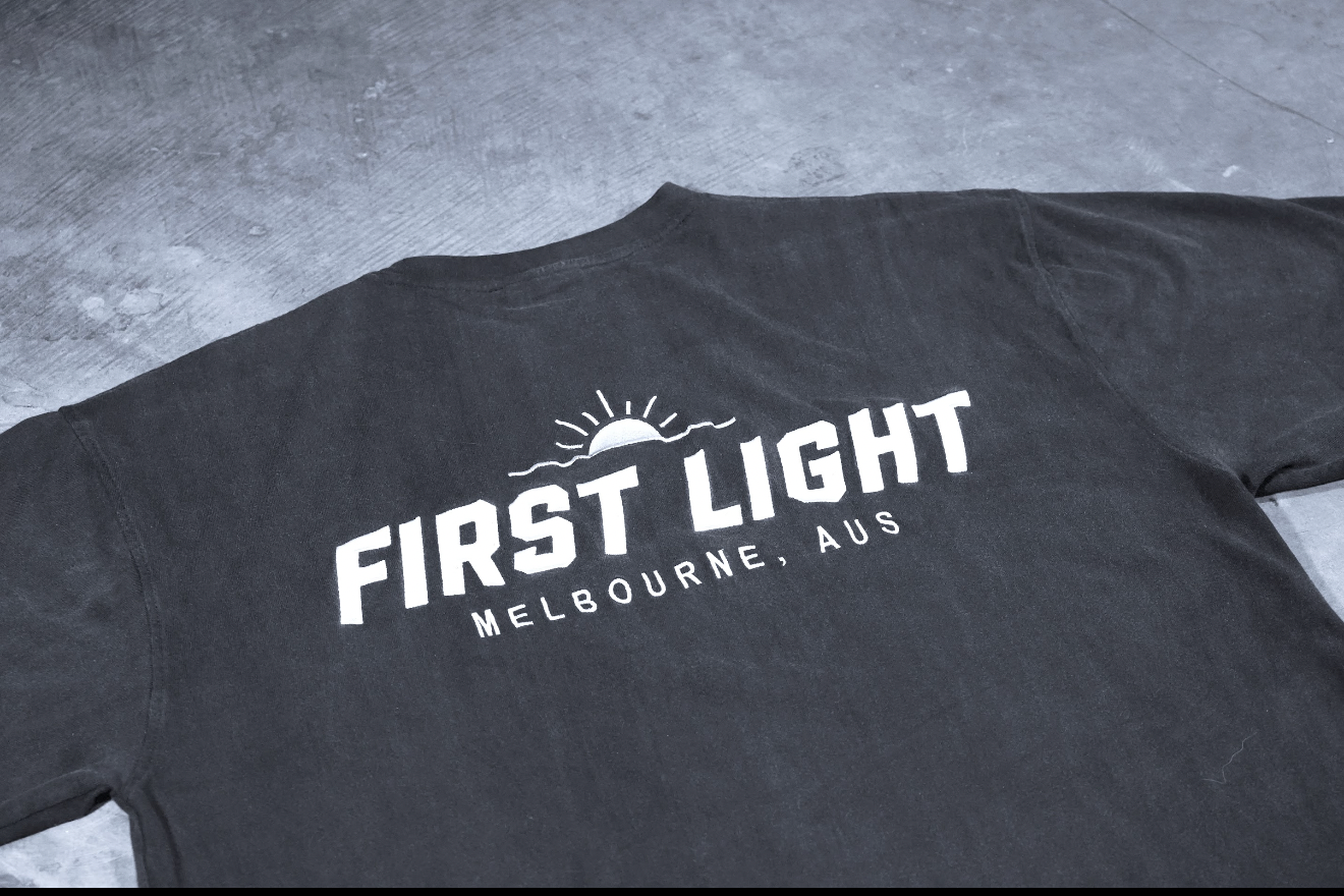 Close-up of the embroidered FIRST LIGHT Melbourne back graphic on the Dawn heavyweight tee