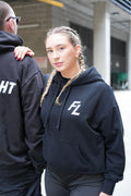 Woman wearing the FIRST LIGHT Dawn heavyweight oversized hoodie in black, embroidered FL chest mark